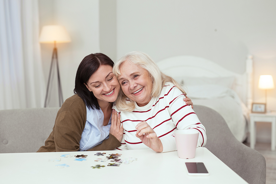 Live-in caregiver offering gentle hand-holding support to senior in bedroom